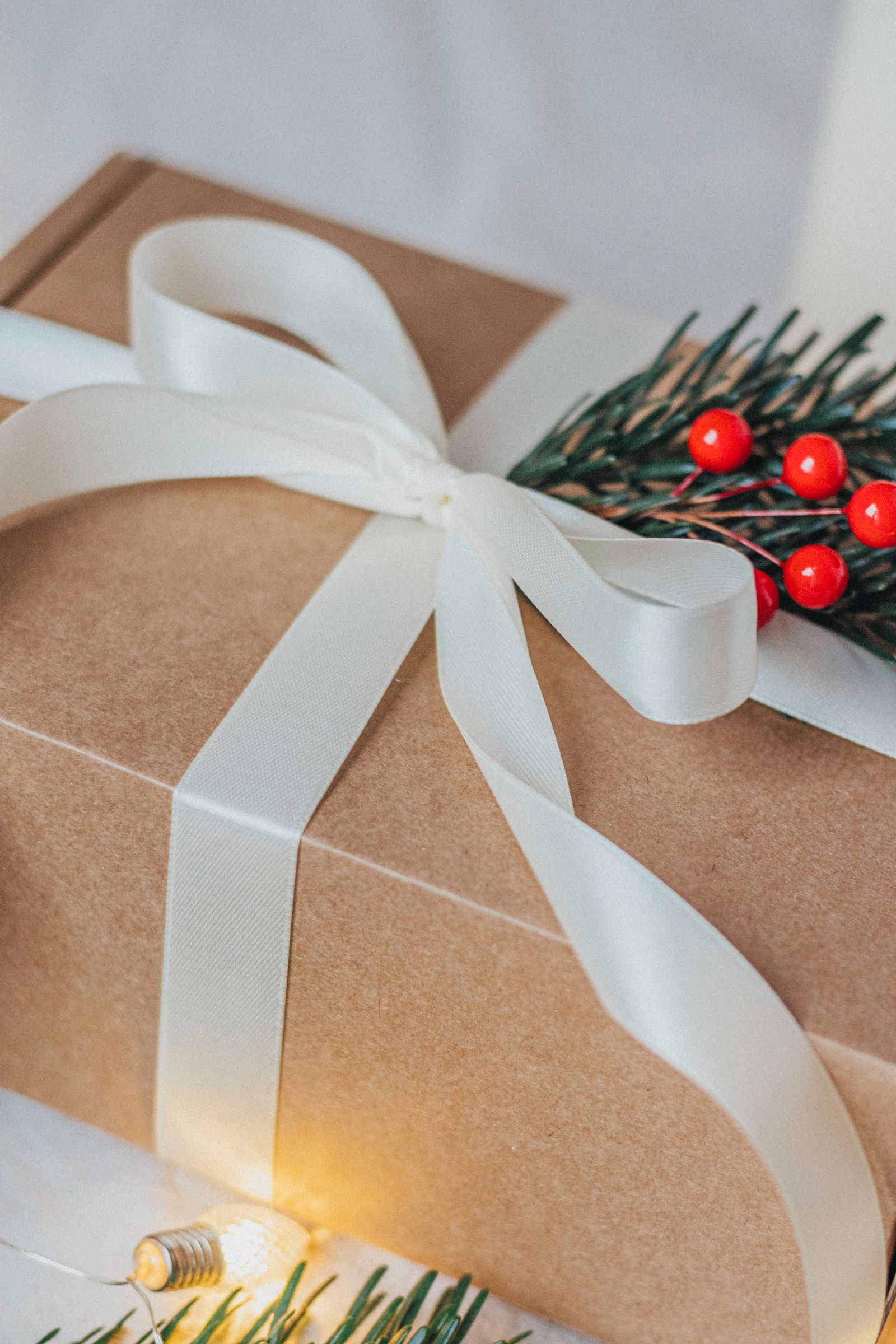 Weihnachtsgeschenk in Kraftpapier mit cremefarbener Schleife, Tannenzweig und roten Beeren