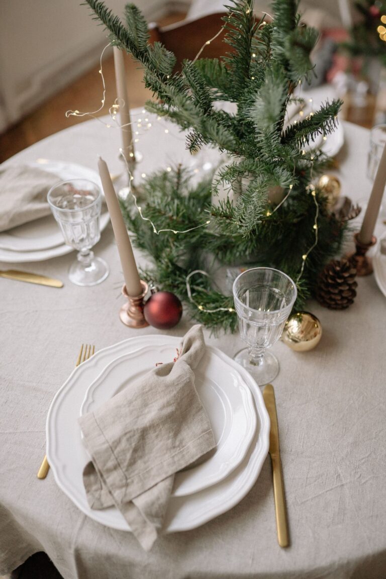 Festlich gedeckter Weihnachtstisch mit Leinentischdecke, goldenem Besteck, Stabkerzen und Tannengrün