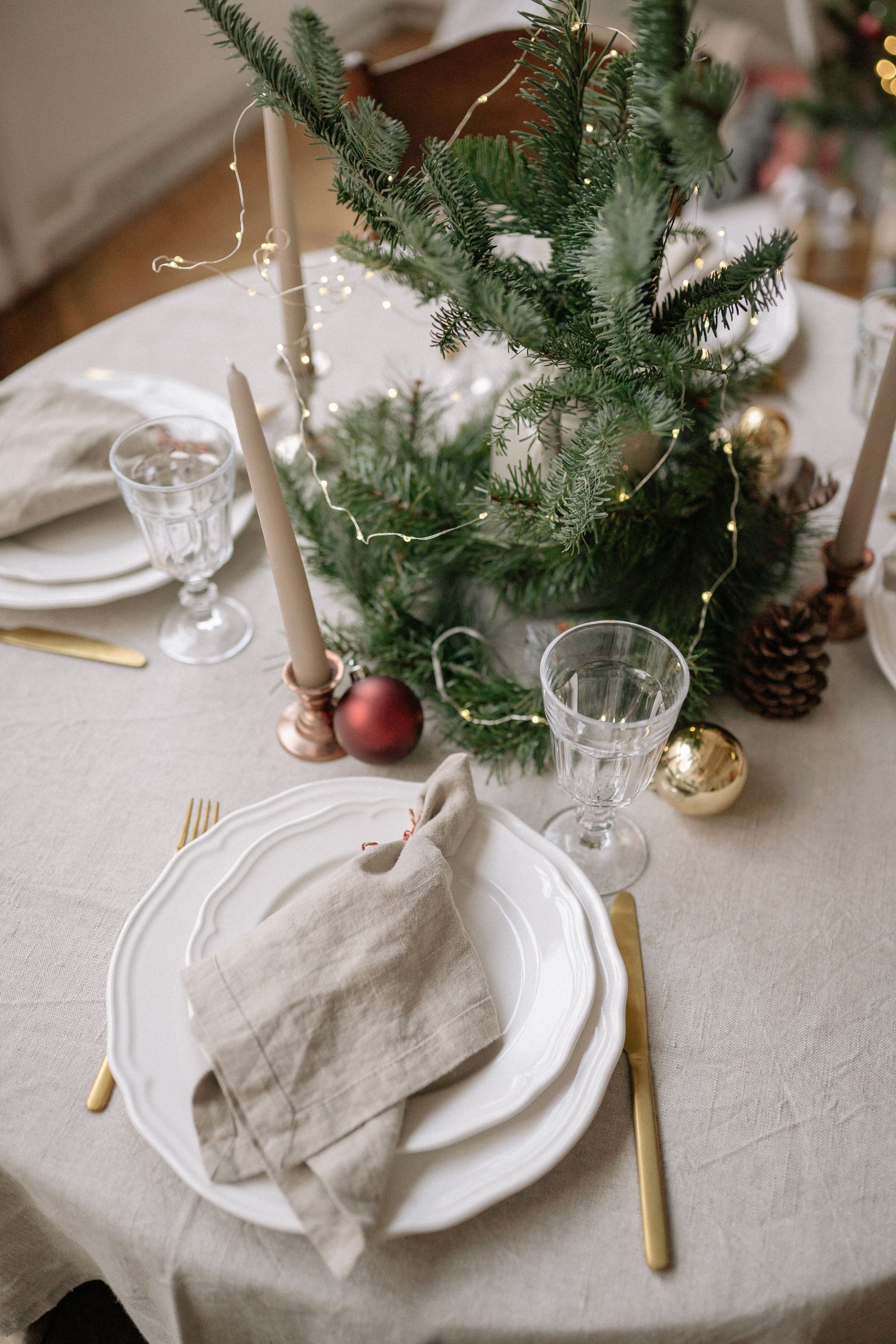 Festlich gedeckter Weihnachtstisch mit Leinentischdecke, goldenem Besteck, Stabkerzen und Tannengrün